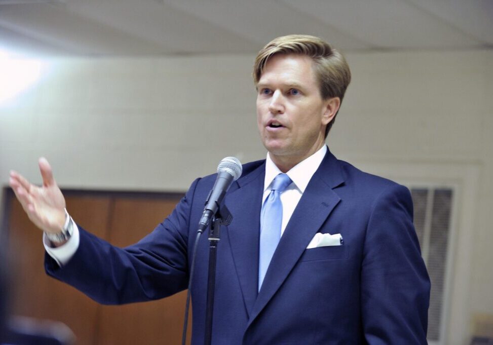 Man speaking at a microphone in suit.
